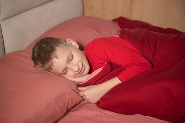 Cute boy in red pajamas sleeping with his eyes closed in bed and smiling