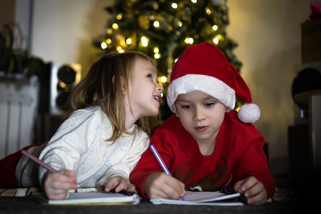 Cute boy in red sweater and red santa hat writes a letter to Santa