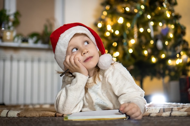 Cute boy in red sweater and red santa hat writes a letter to Santa