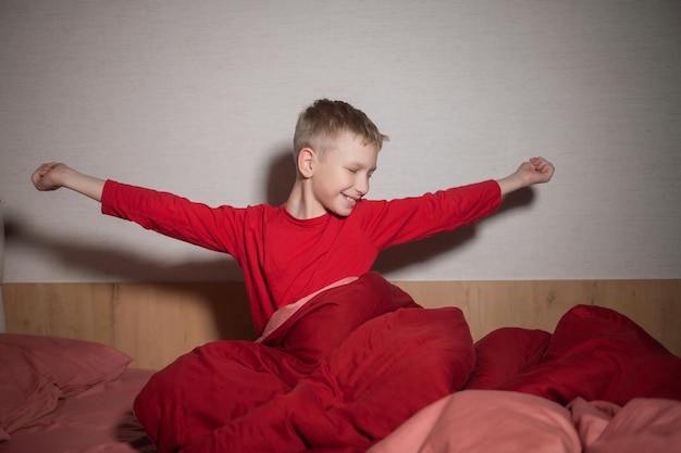 The cute boy sat up on the bed under the blanket and pulled himself up