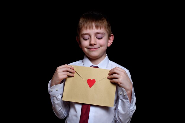 Cute boy in a shirt and tie holds an envelope with a heart. Isolate