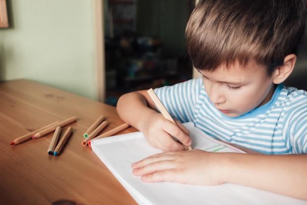 Foto un ragazzo carino si siede alla scrivania e disegna in un album con matite colorate