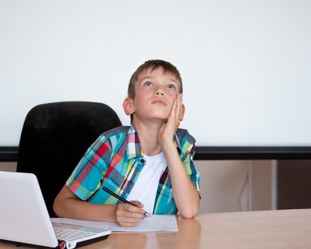 A cute boy sits at the table, looks up, remembers his homework. The boy didn't learn his homework. Concept Back to school, home education, distance education. Copy space