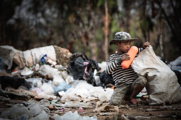 Photo cute boy sitting by garbage outdoors