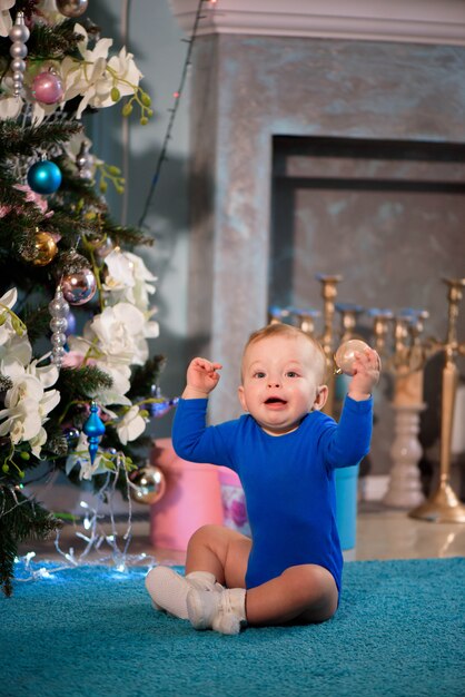 Cute boy sitting on the carpet near Christmas tree