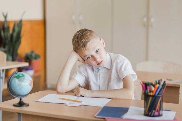 Cute boy sitting at desk in classroom