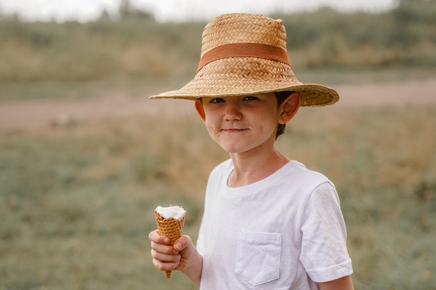 Ragazzo carino con un cappello di paglia mangia il gelato nel villaggio in estate