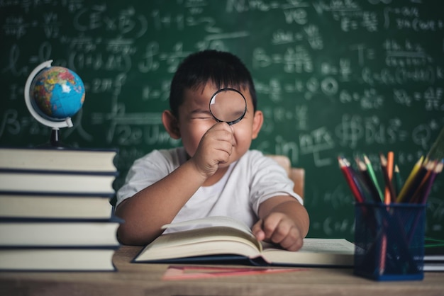 Cute boy studying at table against blackboard