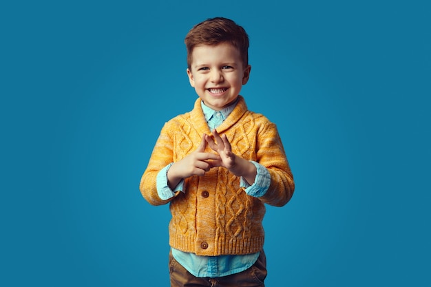 Cute boy in stylish yellow cardigan smiling broadly against blue background