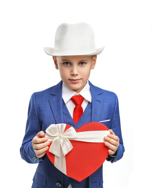 Ragazzo carino in un vestito con una scatola a forma di cuore su uno sfondo bianco