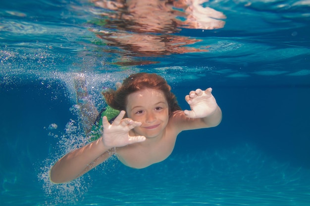 熱帯のビーチで浅いターコイズブルーの海で水中を泳ぐかわいい男の子子供が泳ぎ、水中に飛び込む