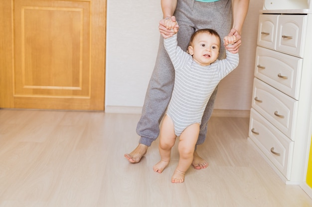 Cute boy taking first steps holding mother's hands.