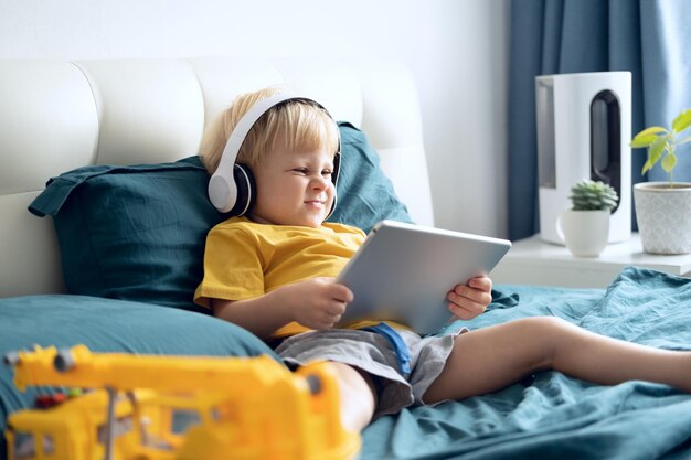 Cute boy using digital tablet while sitting on bed at home