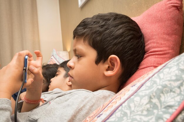 Photo cute boy using mobile phone while lying by siblings at home