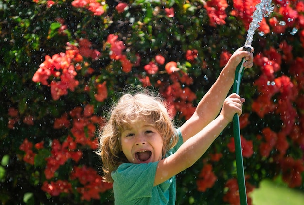 Cute boy watering plants in the garden at summer day child with garden tools and watering hose in ba