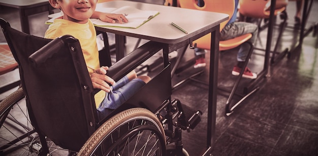 Foto ragazzo carino sulla sedia a rotelle seduto in classe