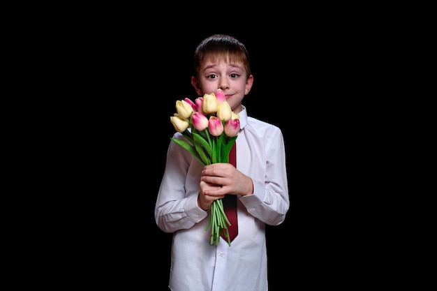 Ragazzo carino in camicia bianca con un bouquet di tulipani isolare su sfondo nero