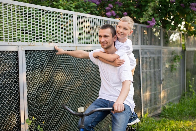 A cute boy in a white Tshirt rides a bike with his dad and laughs