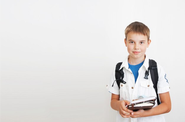 Cute boy with a backpack on a gray background with copy space. In the hands of notebooks and a medical mask. Learning, education, school concept