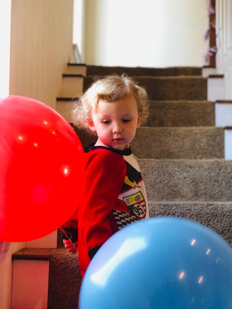 Cute boy with balloons standing on steps at home