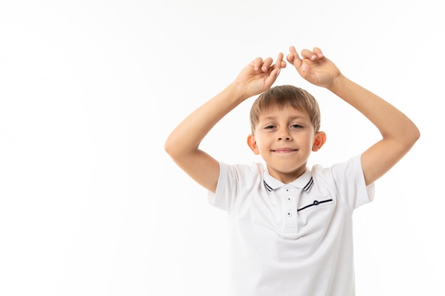 Cute boy with bangs in a white T-shirt and glasses with crossed fingers on white