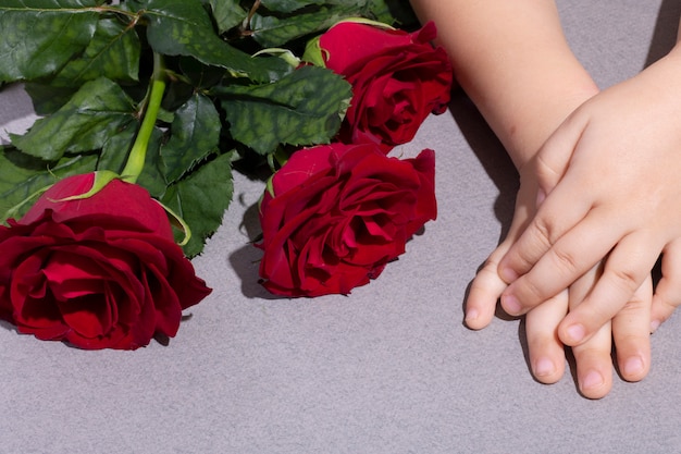 Cute boy with bouquet of beautiful red roses on table, top view