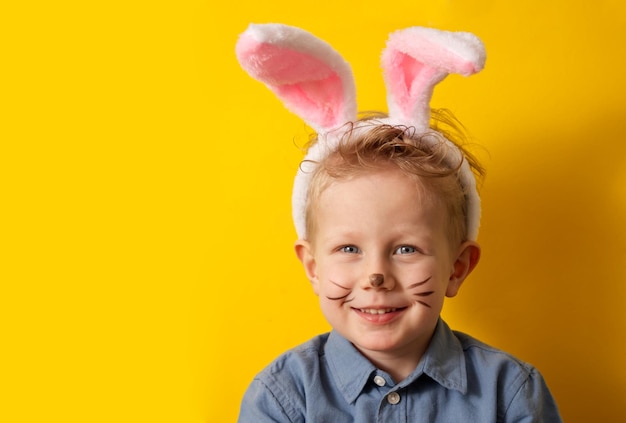 Симпатичный мальчик с кроличьими ушами улыбается на желтом фоне