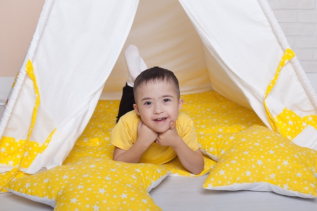 Cute boy with Down syndrome sitting in a yellow hut