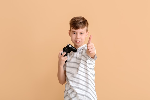 Cute boy with game pad showing thumb-up on color background