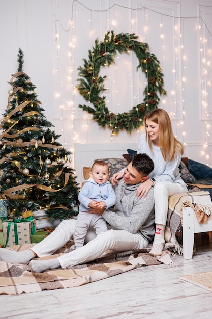 Cute boy with happy parents near the Christmas tree A family with a small child in a bedroom near a decorated Christmas tree Festive New Year's atmosphere Family celebration