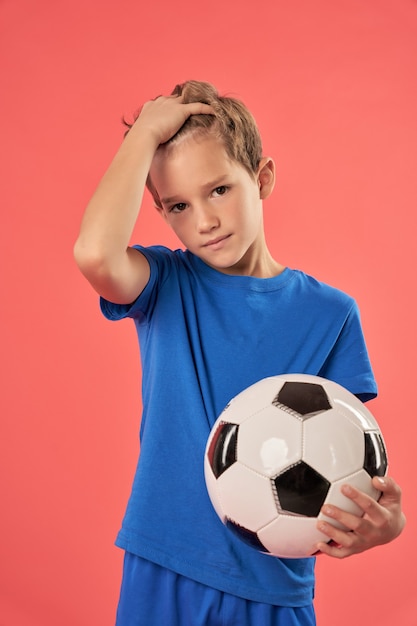 Cute boy with soccer ball standing against red background