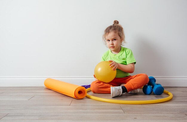 Cute boy with sport equipment sitting on a floor