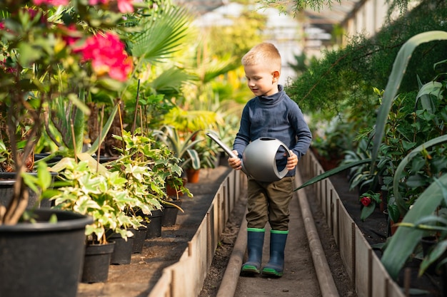 Cute boy with watering can in greenhouse