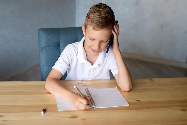cute boy writes in an open notebook and looks at the phone talking on the phone