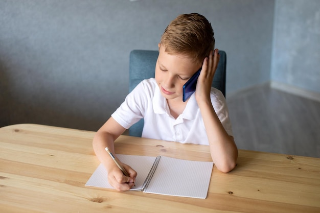 cute boy writes in an open notebook and looks at the phone talking on the phone