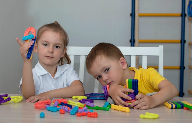 Cute brother and sister play with toy constructor on the table in the room. The concept of sibling bonding, friendship, and learning through play activities for child development.