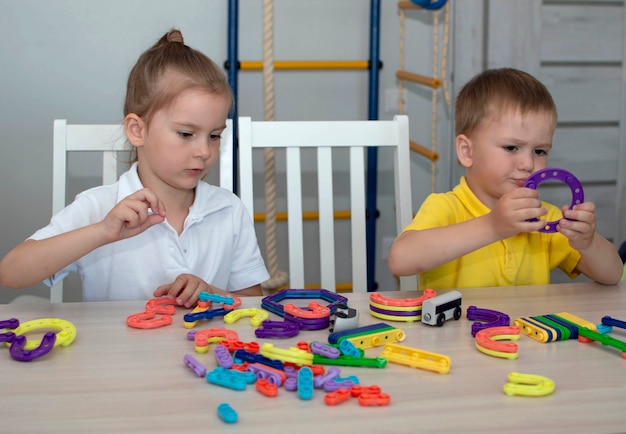 かわいい兄と妹は部屋のテーブルでおもちゃのコンストラクターで遊んでいます。兄弟の絆、友情、そして子どもの発達のための遊び活動を通して学ぶという概念。