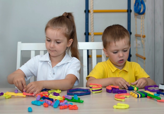 Cute brother and sister play with toy constructor on the table in the room. The concept of sibling bonding, friendship, and learning through play activities for child development.