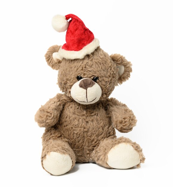 Cute brown teddy bear sitting in red christmas cap on white  background