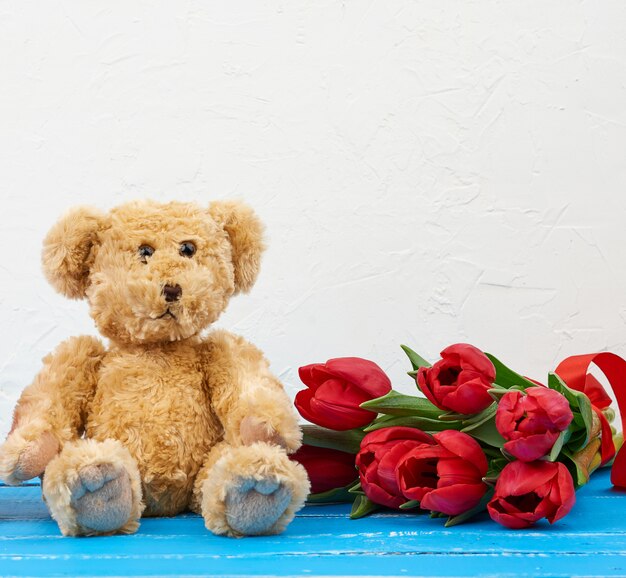 Cute brown teddy bear with bouquet of red tulips