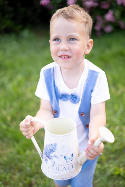 写真 夏に青い目をしたかわいい茶色の髪の赤ちゃん子供が笑う明るい晴れた日は、じょうろを持ち、自然の世話をする花に水をまきます