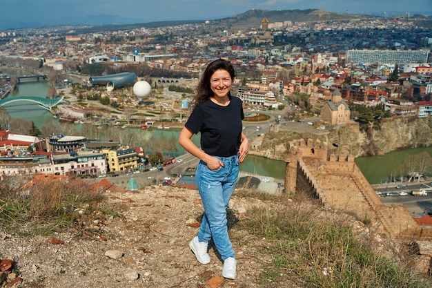 A cute brunette girl enjoys the stunning scenery of Tbilisi from the hill. The whole city at her feet.