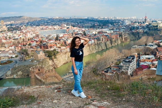 A cute brunette girl enjoys the stunning scenery of Tbilisi from the hill The whole city at her feet