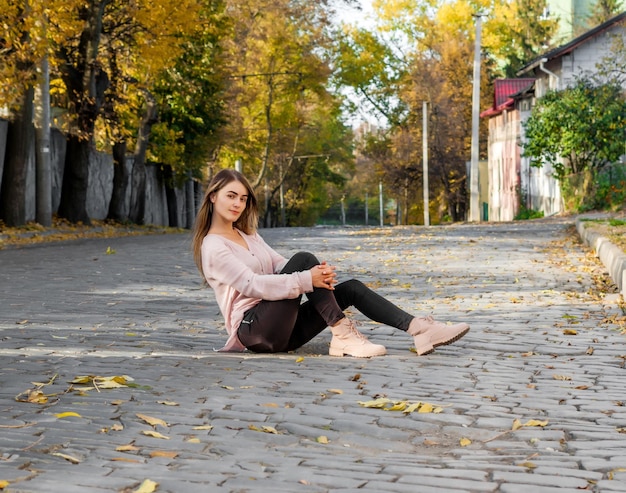 Cute brunette girl sits on a road enclosed paving stone Autumn the city