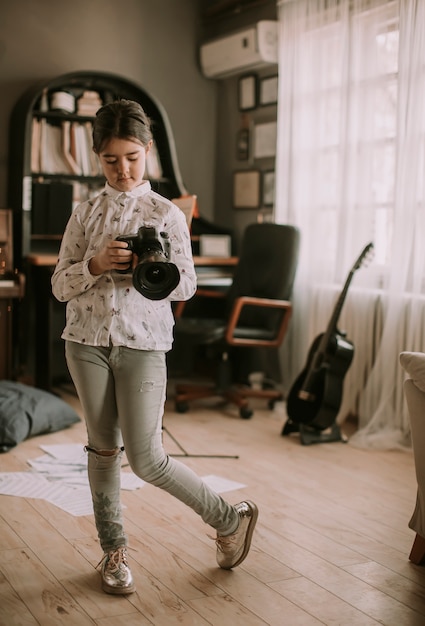 Cute brunette little girl holding a photo camera in the room