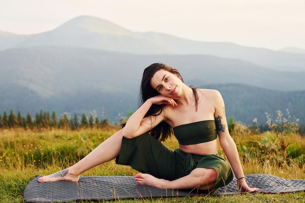 Photo cute brunette sits on yoga mat majestic carpathian mountains beautiful landscape of untouched nature