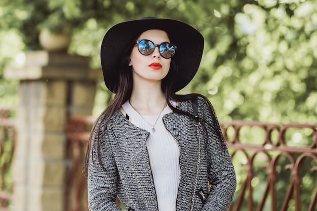 Cute brunette with red lips in hat and sunglasses posing in city 