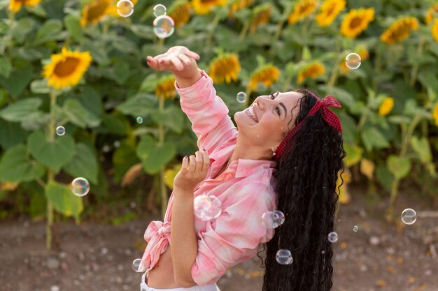 Cute brunette woman blowing soap bubbles. Beautiful field with sunflowers on background.