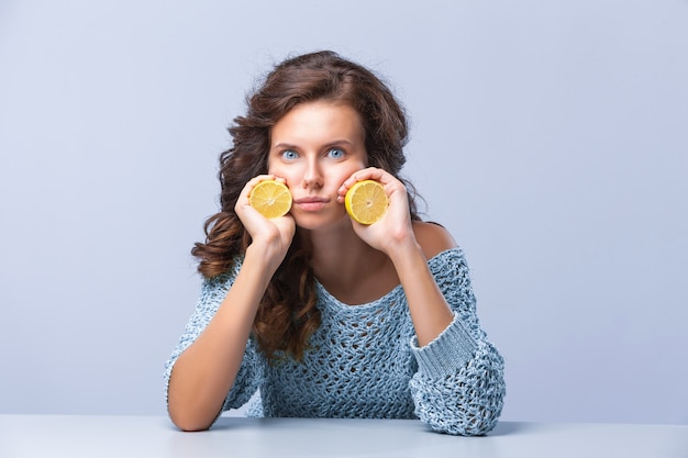 Cute brunette woman holding two halves of yellow lemon citrus fruit in hands with sad face emotion