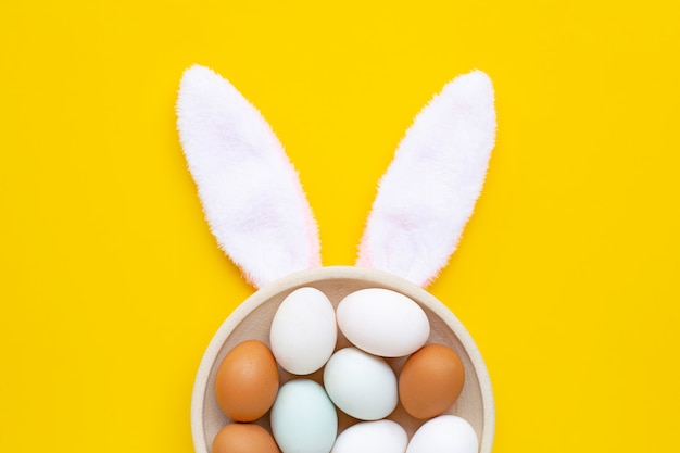 Симпатичные уши кролика с яйцами на желтом фоне. Пасхальный